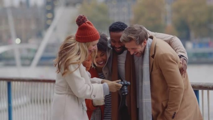 一群朋友在户外穿着外套和围巾在伦敦秋冬之旅的相机上摆姿势拍照-慢动作拍摄