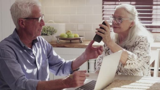 一对高级夫妇坐在家里的厨房里使用技术的4k视频片段