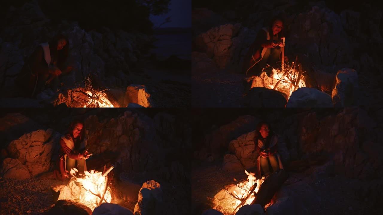 年轻女子晚上将树枝放在篝火中