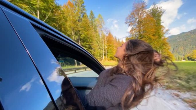 女人开车穿过五颜六色的秋天森林时玩得开心