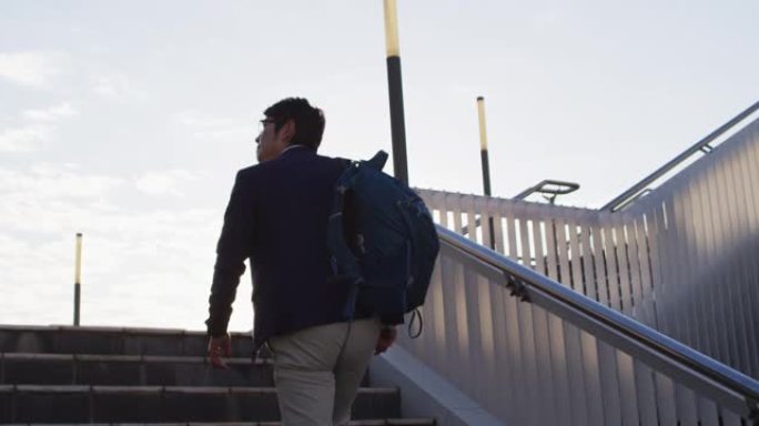 亚洲男子背着背包在公司公园爬楼梯