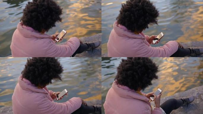 年轻女子坐在城市公园的池塘边玩手机