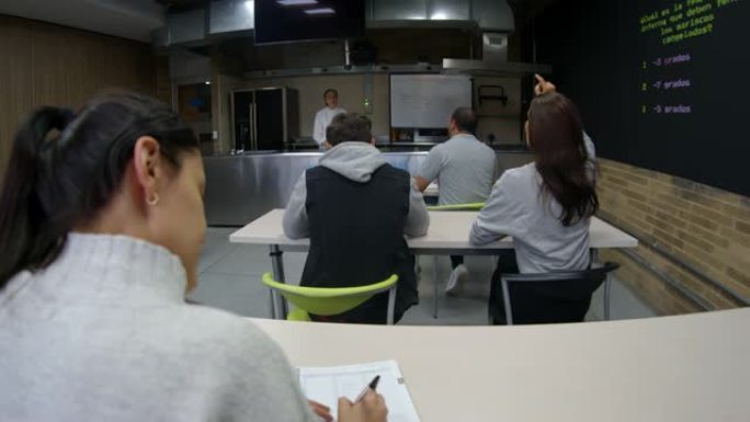 理论课上烹饪学生的后视图向教室前面的女老师提问