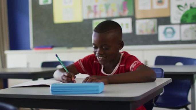 快乐的非洲裔美国小学生坐在教室里做笔记，看着相机的肖像