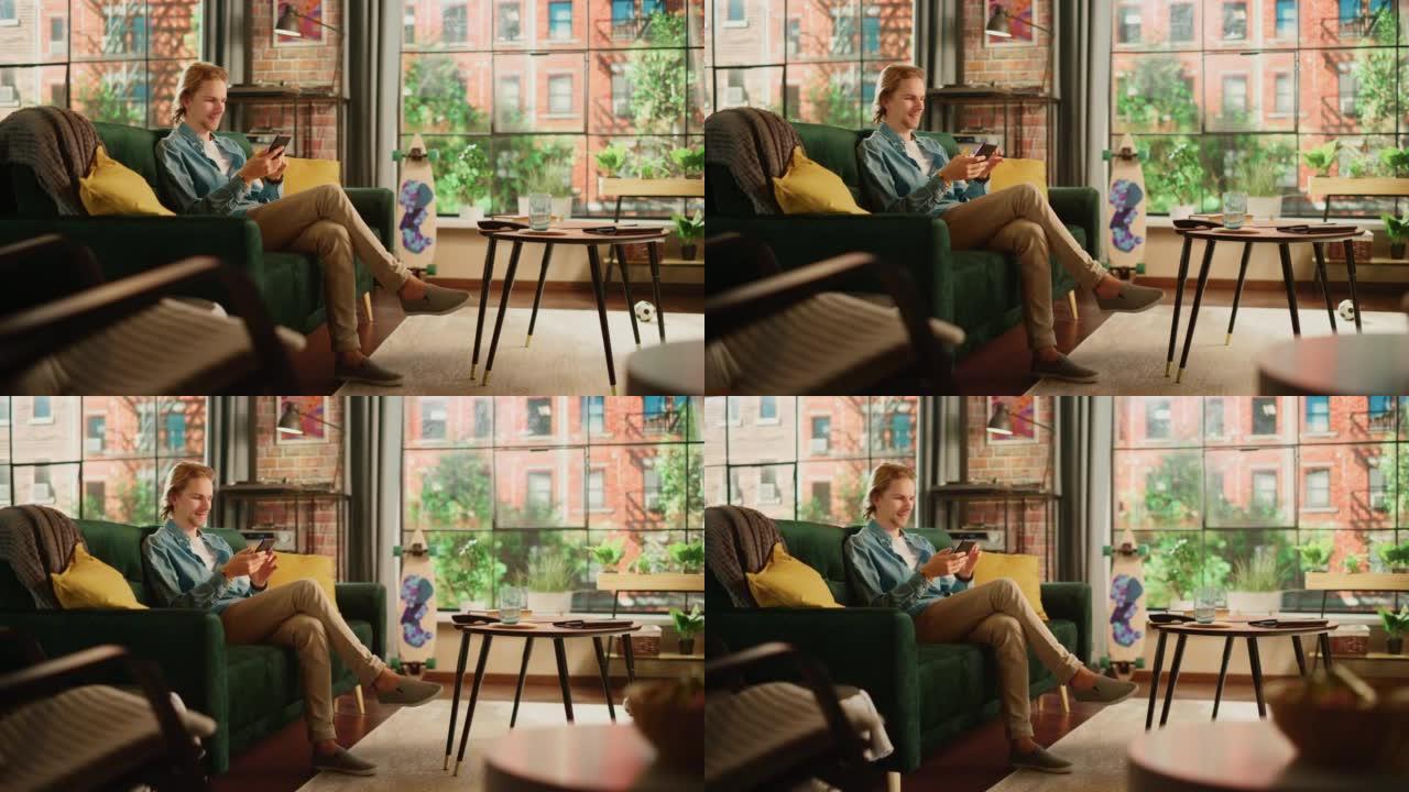 年轻英俊的成年男子坐在阁楼公寓的沙发上，放松并使用智能手机。有创意的男性检查社交媒体，与朋友聊天，浏