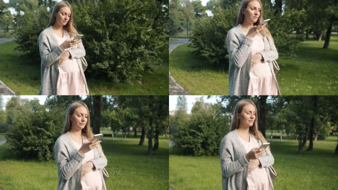 年轻怀孕的金发女郎走在城市公园用智能手机录制音频信息