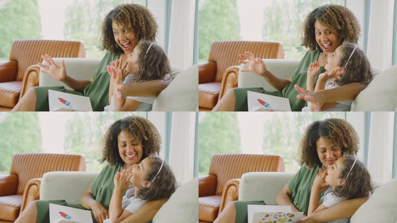 笑着的母女俩坐在家里的沙发上一起看书-慢动作拍摄