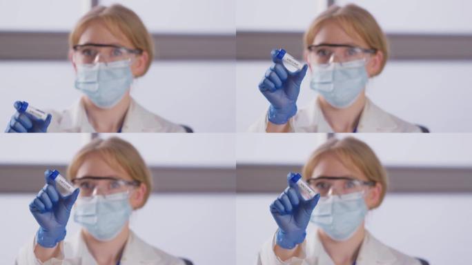女实验室研究人员穿着个人防护用品，手持标有疫苗的试管