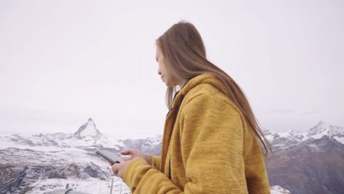 穿着冬季夹克的年轻女性在瑞士马特宏峰 (Matterhorn Peak) 上使用电话。体验旅行与多样