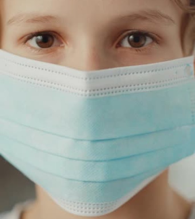 小男孩在室内戴防护口罩的垂直格式视频。棕色眼睛的金发男性尊重检疫规则、封锁措施和安全的社交距离。大流