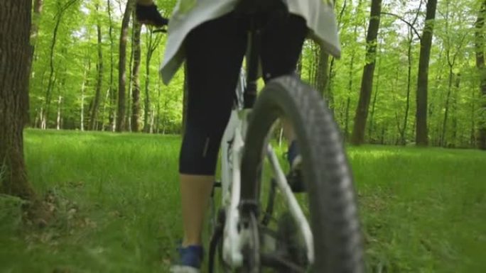 SLO MO女人骑着山地自行车穿过森林中的林间空地