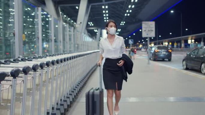 亚洲商务女孩到达目的地戴着口罩，带着行李在国内机场候车厅外行走。