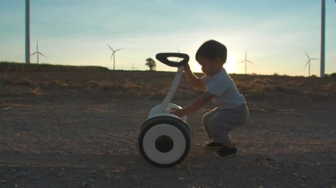 17个月大的男婴的剪影日落在风车农场学习和对电动踏板车的好奇心，用于能源生产，婴儿技术的未来。替代生
