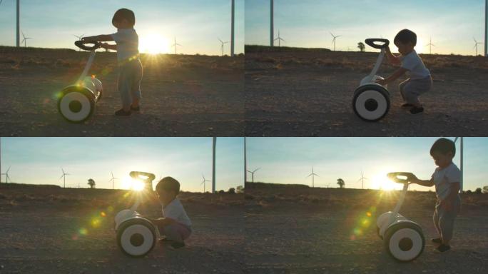17个月大的男婴的剪影日落在风车农场学习和对电动踏板车的好奇心，用于能源生产，婴儿技术的未来。替代生