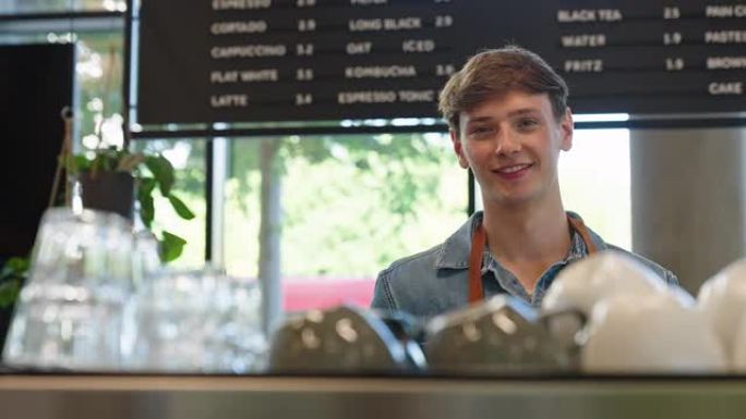 快乐的年轻男咖啡师站在咖啡店柜台后面