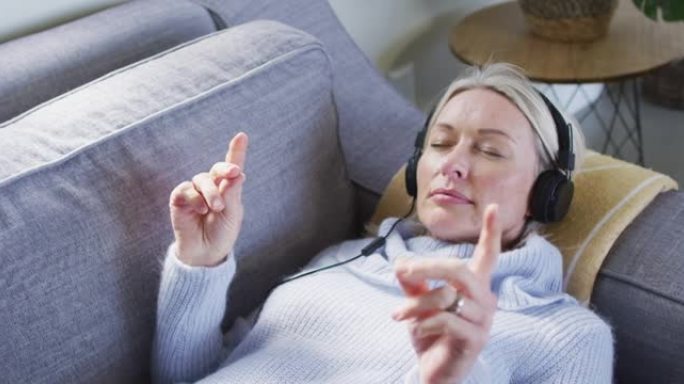 客厅里放松的白人女性躺在沙发上，戴着耳机