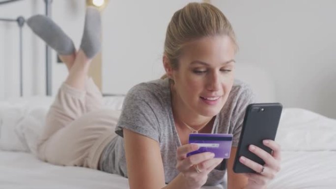 女人躺在床上用手机上网购物用信用卡穿睡衣