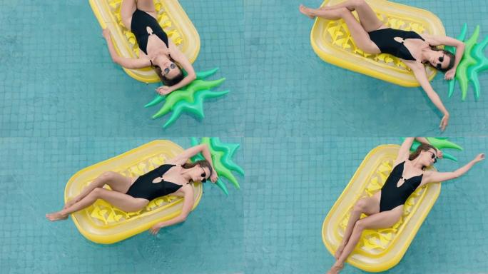 迷人的女人在充气菠萝漂浮在游泳池里享受夏天，穿着性感比基尼度假放松