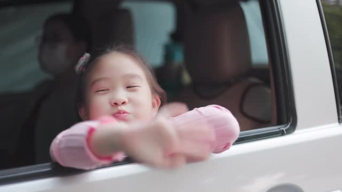 可爱的亚洲小女孩在汽车座椅后部挥手告别