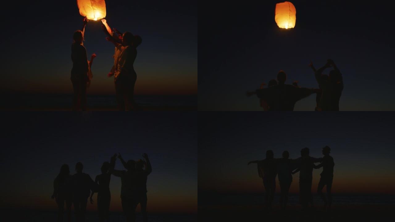 一群年轻朋友的慢动作剪影很高兴在日落时站在海滩上放下天灯。