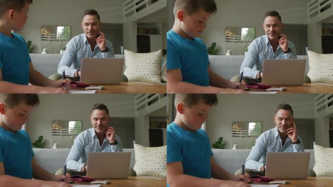 快乐的高加索父亲，儿子坐在餐桌旁，在家用笔记本电脑学习