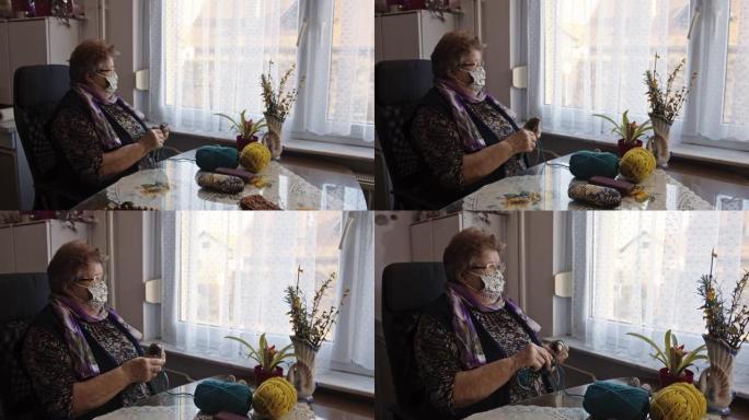 老妇人戴着防护口罩，透过窗户向外看时编织