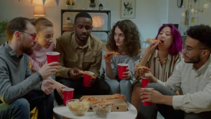 在黑暗公寓的派对上吃披萨和享受饮料的多元文化朋友