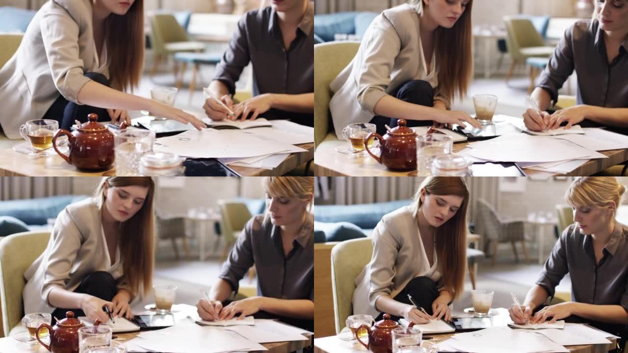 两个迷人的女商人坐在咖啡馆里并通过文书工作的4k视频片段