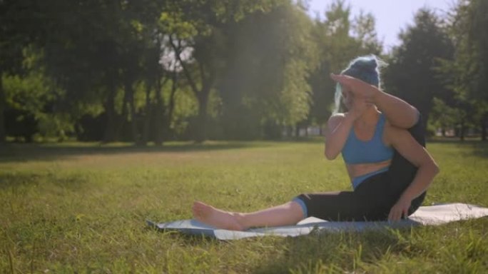 一个年轻迷人的绿松石头发的女人在阳光下在公园的瑜伽垫上锻炼