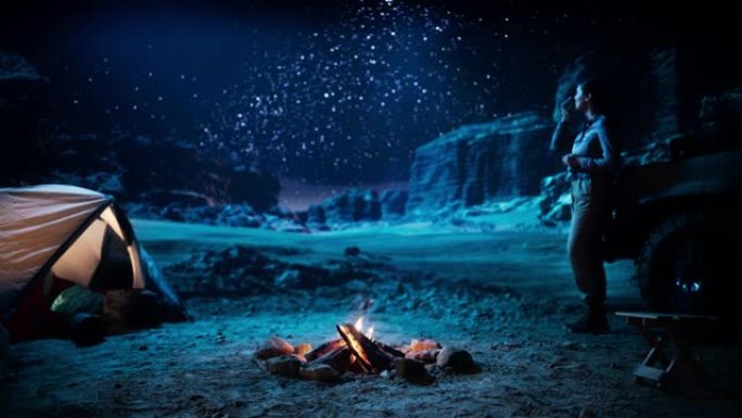 女性旅行者在篝火旁露营时看着夜空。银河系星星的惊人营地景观，有权力的女冒险家热爱自然旅行
