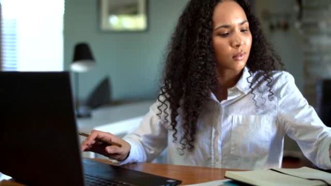 紧张的女商人在使用电话通话时在笔记本电脑上写字并在笔记本电脑上工作。一位女性商业专业人士，在手机上聊