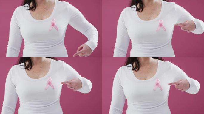 一个女人的中间部分指向粉红色背景下胸前的粉红色丝带