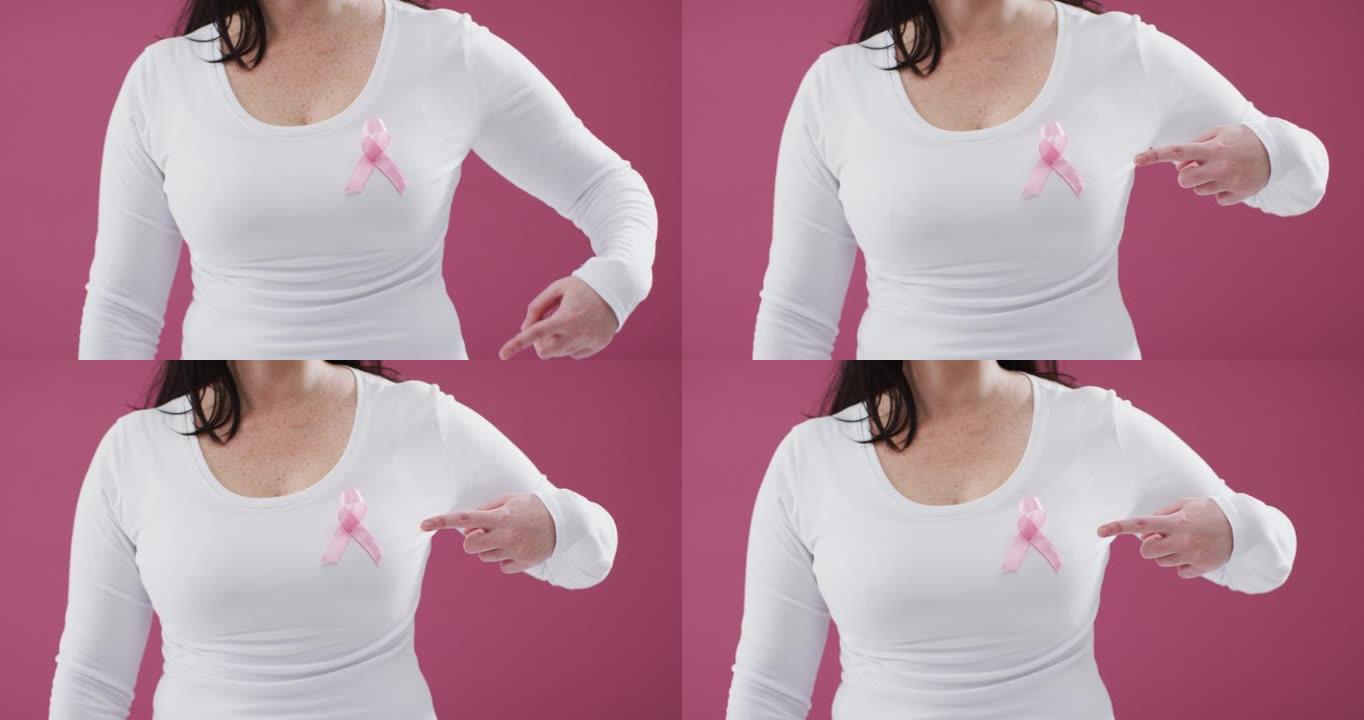 一个女人的中间部分指向粉红色背景下胸前的粉红色丝带