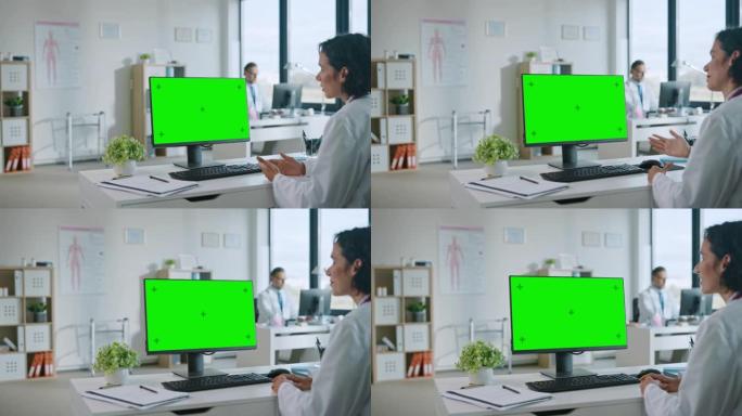 女医生正在健康诊所的绿屏模拟显示的计算机上与患者进行视频通话。穿着实验室外套的助理正在医院办公室谈论
