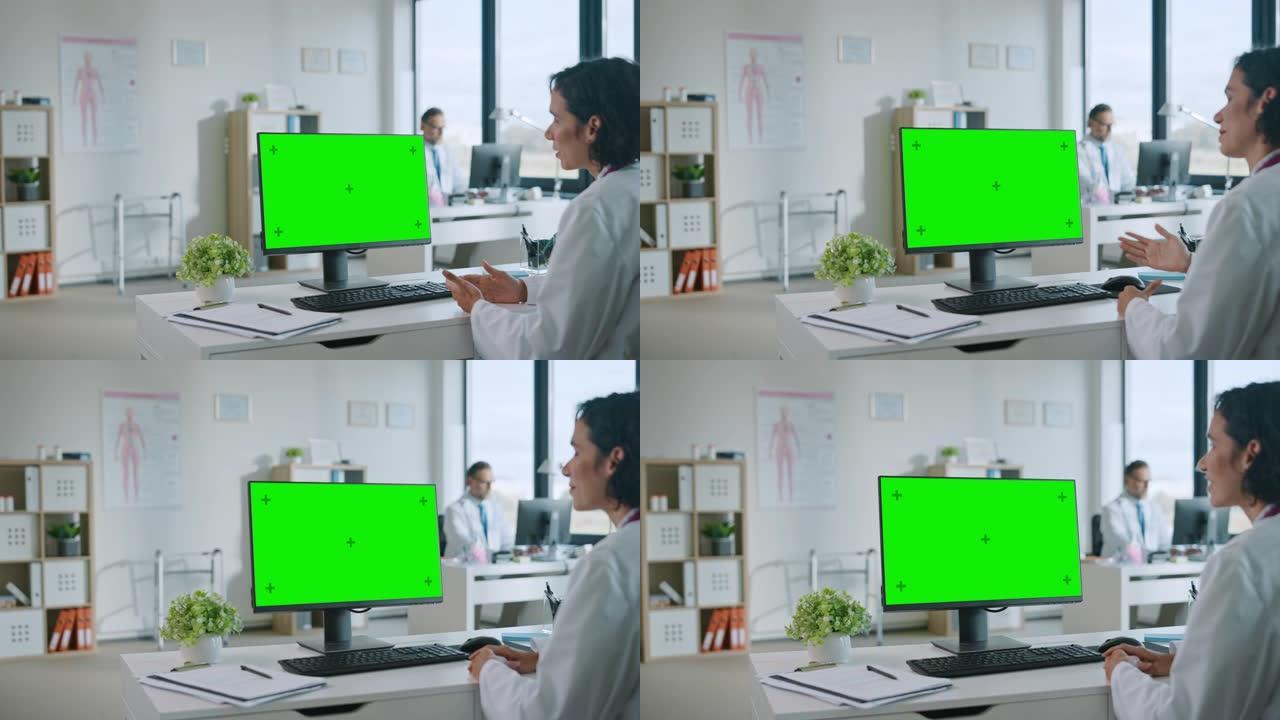 女医生正在健康诊所的绿屏模拟显示的计算机上与患者进行视频通话。穿着实验室外套的助理正在医院办公室谈论