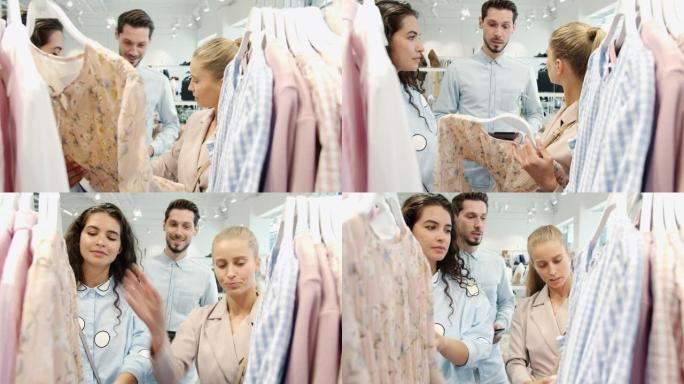 年轻女性朋友选择衣服并与商店里拿着平板电脑的推销员交谈