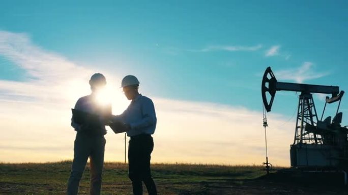 在明亮的夕阳下，两名石油工人在油田里交谈