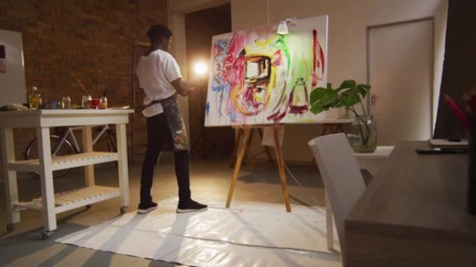 非裔美国男艺术家在艺术工作室穿着围裙画，用调色板刀在画布上