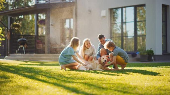 美丽的微笑四口之家在后院草坪上拥抱快乐的金毛猎犬。田园诗般的家庭在避暑别墅后院户外拥抱忠诚的血统狗。