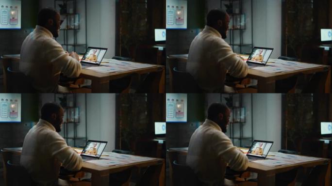 英俊的黑人非洲裔美国项目经理正在创造性的办公环境中使用笔记本电脑进行视频通话。男性专家通过实时摄像机