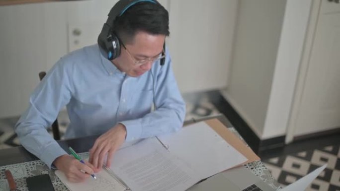 高角度亚洲中国中年男子早上在厨房用笔记本电脑上在线课