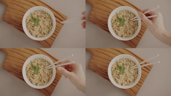 拉面菜用筷子和手放木棍煮熟的方便面的俯视图