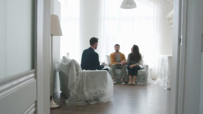 顾客年轻夫妇在新房室内与房地产经纪人交谈