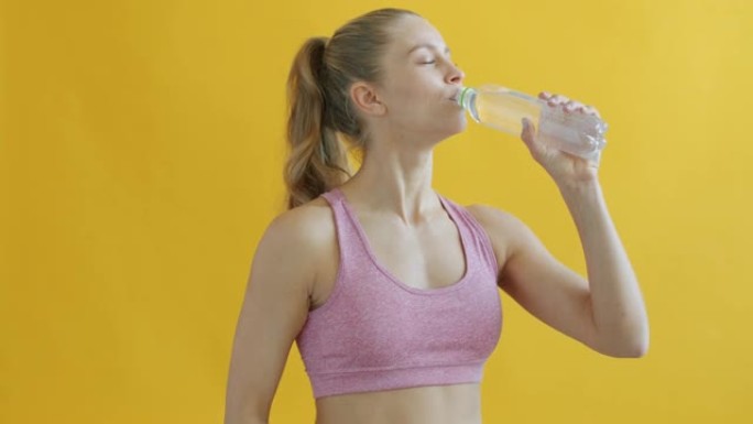 穿着运动服的年轻女士的肖像从瓶子里喝水看着相机，微笑着