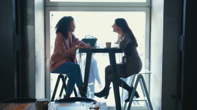 侧视图两个快乐美丽的多民族女性朋友在咖啡店见面。团结和友谊的概念。