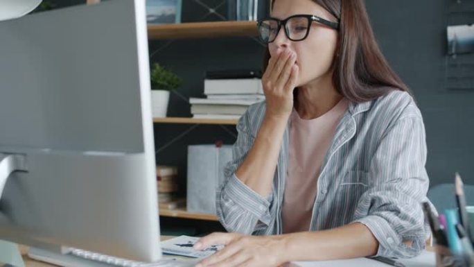 年轻女商人在家用电脑打哈欠感到疲倦的慢动作肖像