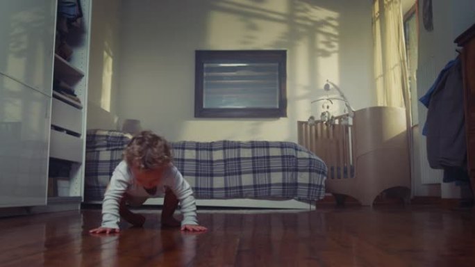 电影拍摄的快乐微笑的赤脚小男孩穿着浅蓝色的身体，正在家里的木地板上迈出第一步。概念: 生活，童年，真