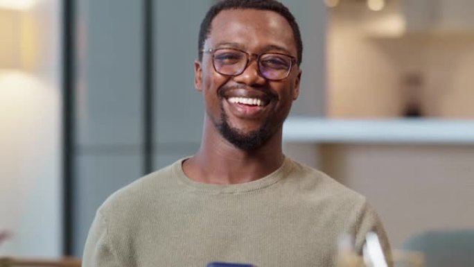 肖像快乐英俊的黑人男子在家里微笑。年轻的非洲裔美国企业家使用他的智能手机。在他的手机上浏览一些在线购