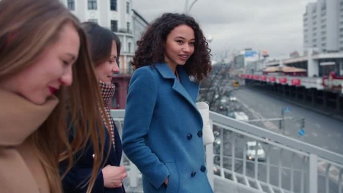 侧视图三个快乐的年轻多民族女性朋友沿着城市大桥漫步，随意聊天，女孩权力概念。