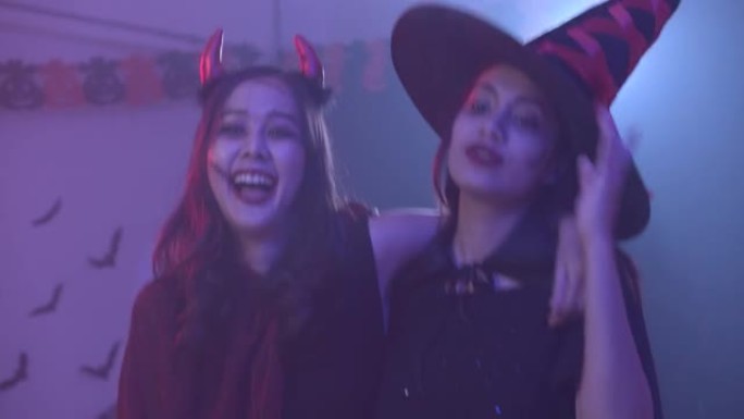 两位穿着万圣节服装的迷人亚洲女士随着音乐跳舞，在五颜六色的紫外线霓虹灯背景下一起玩乐派对。女人享受夜